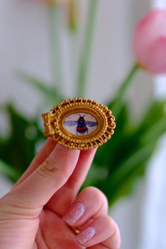 Hand holding a decorative object with a bee design against a blurred floral background